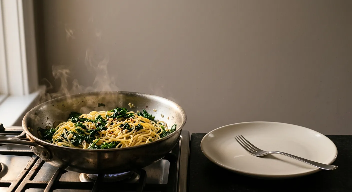 A pan of pasta, greens and garlic on a weeknight stove